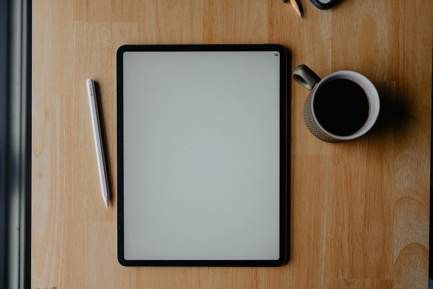 A tablet with a stylus and coffee mug on a table.