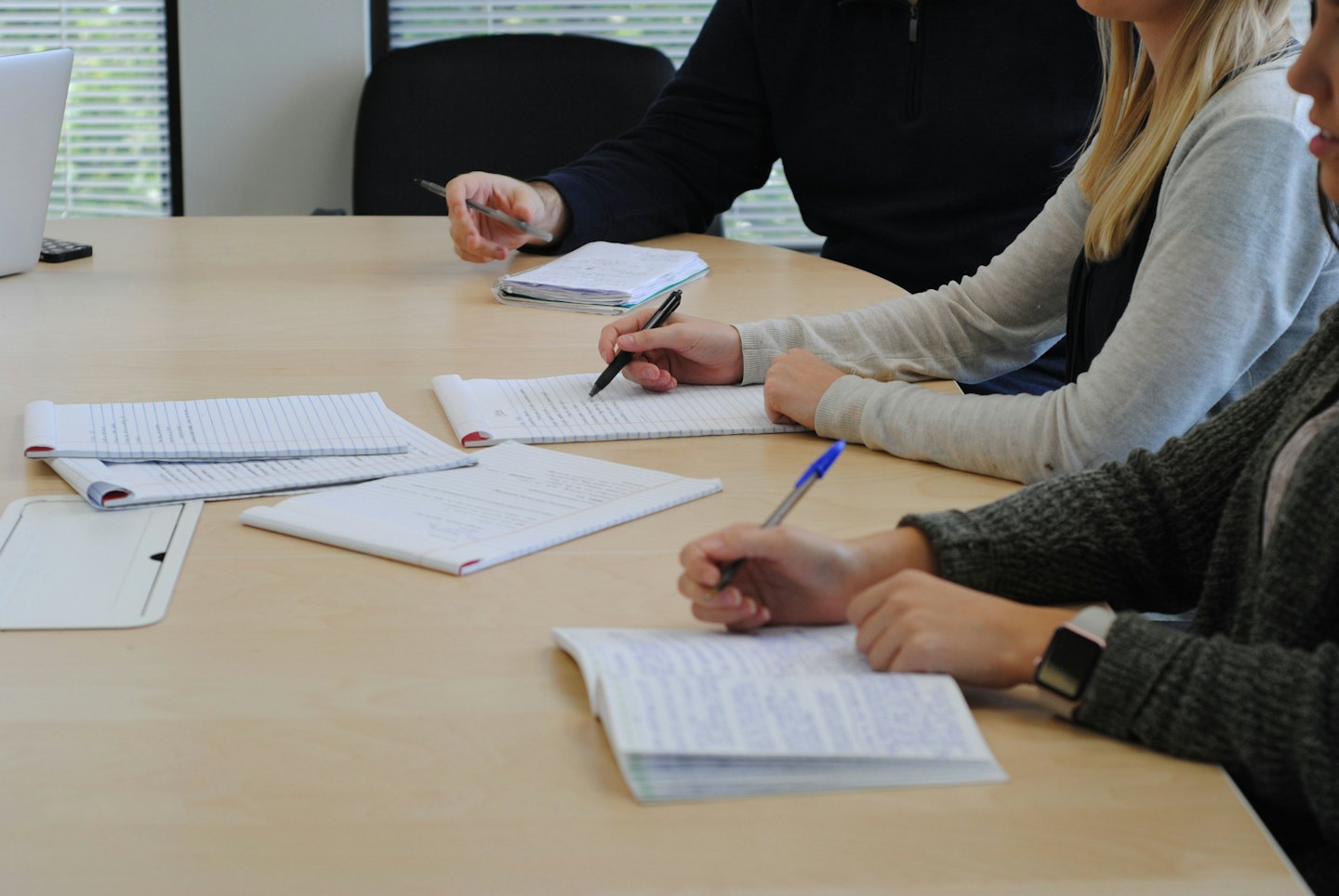 Three people collaborating and taking notes in notebooks.